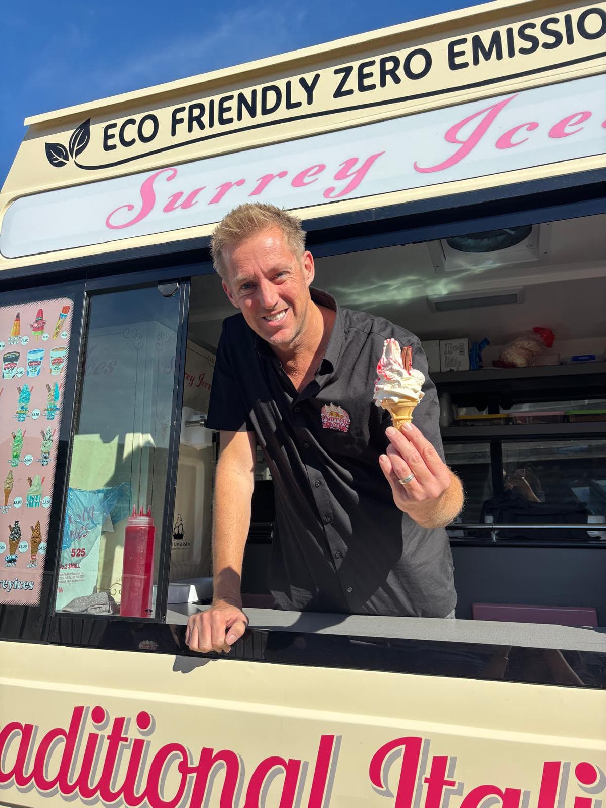 A Hampshire Ices server leaning from the hatch of an eco-friendly van, holding a soft serve cone