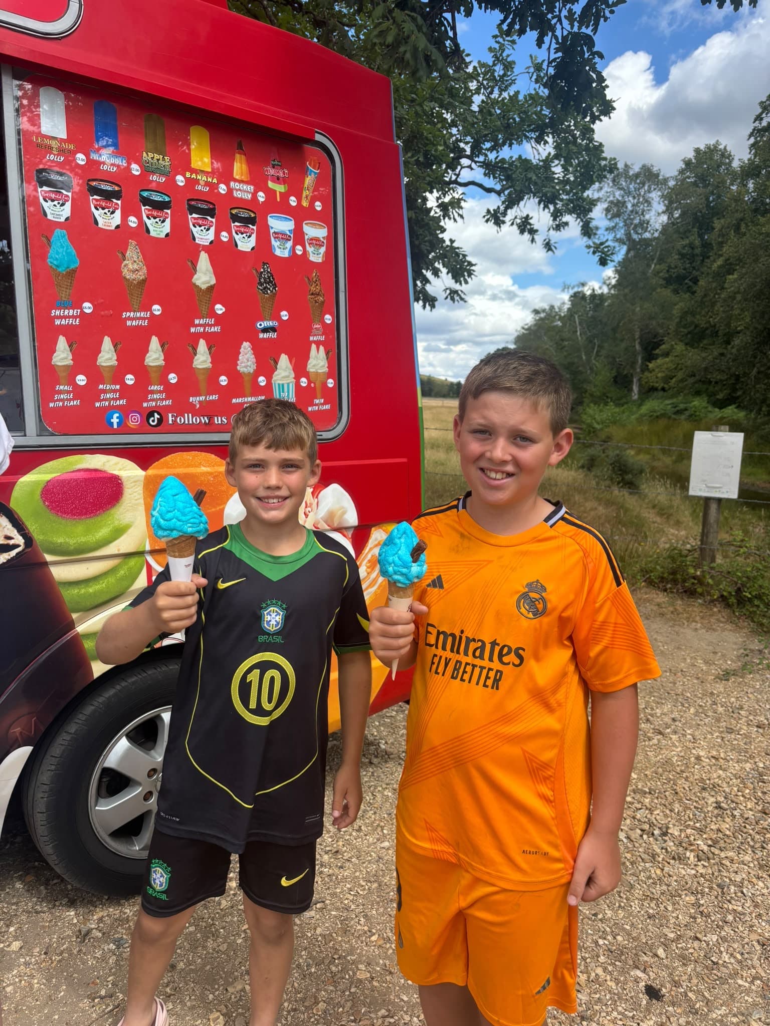 Two boys holding bright blue ice cream cones beside a red ice cream van