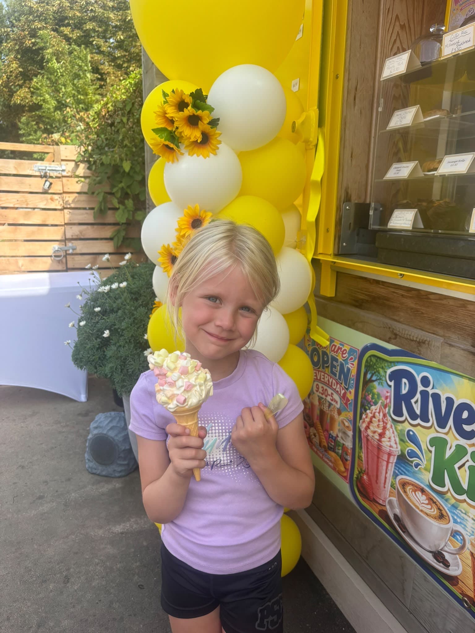 A girl holding a cone topped with marshmallows beside yellow and white balloons